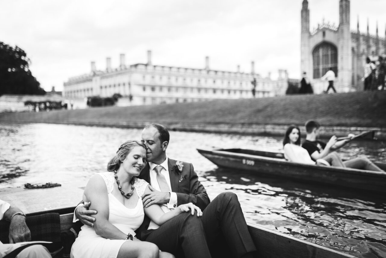 A married couple punting on the River Cam with their Cambridge wedding venue in the background.