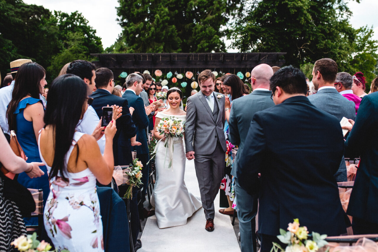 A couple walk back up the aisle in their outdoors wedding ceremony at Swynford Manor.