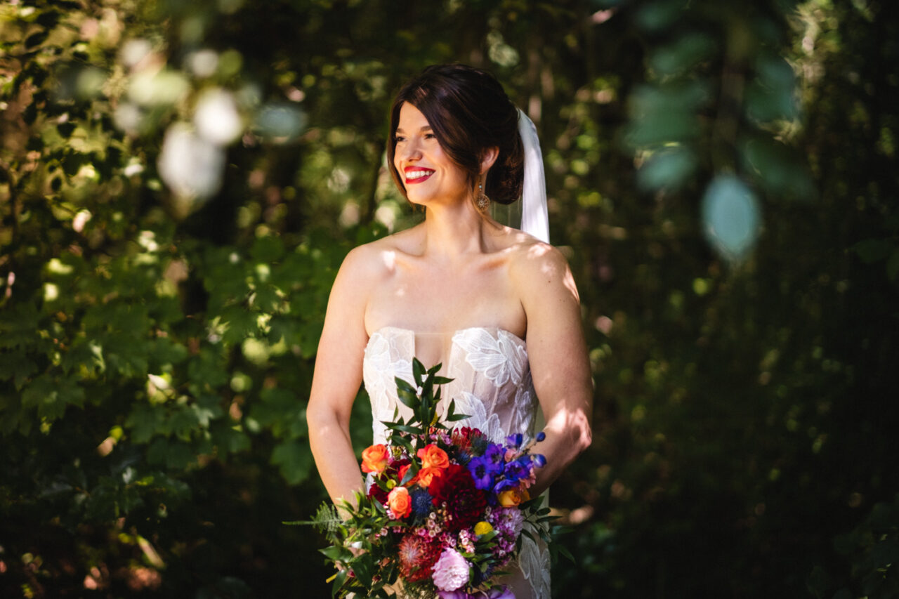 A bride poses for a photo with beautiful woodlands behind her in dappled light.