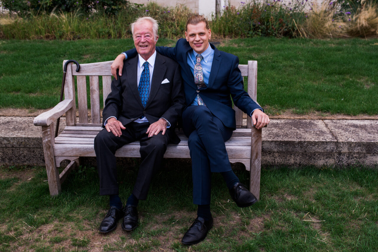 Two wedding guests sit on a bench.