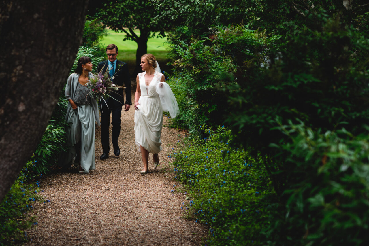 A bride and her father and her bridesmaid walking in the grounds of Downing College.