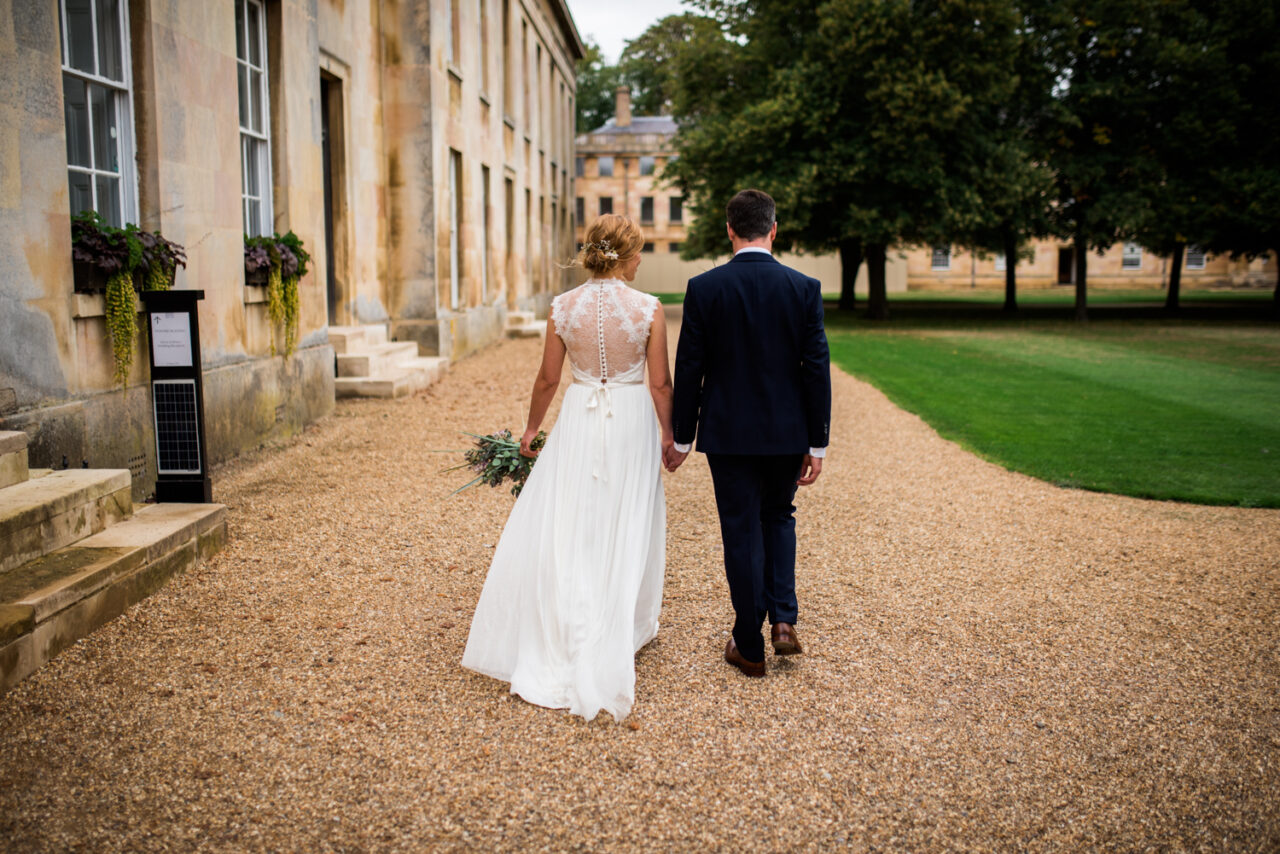 A bride and groom walk in the grounds of Downing College.