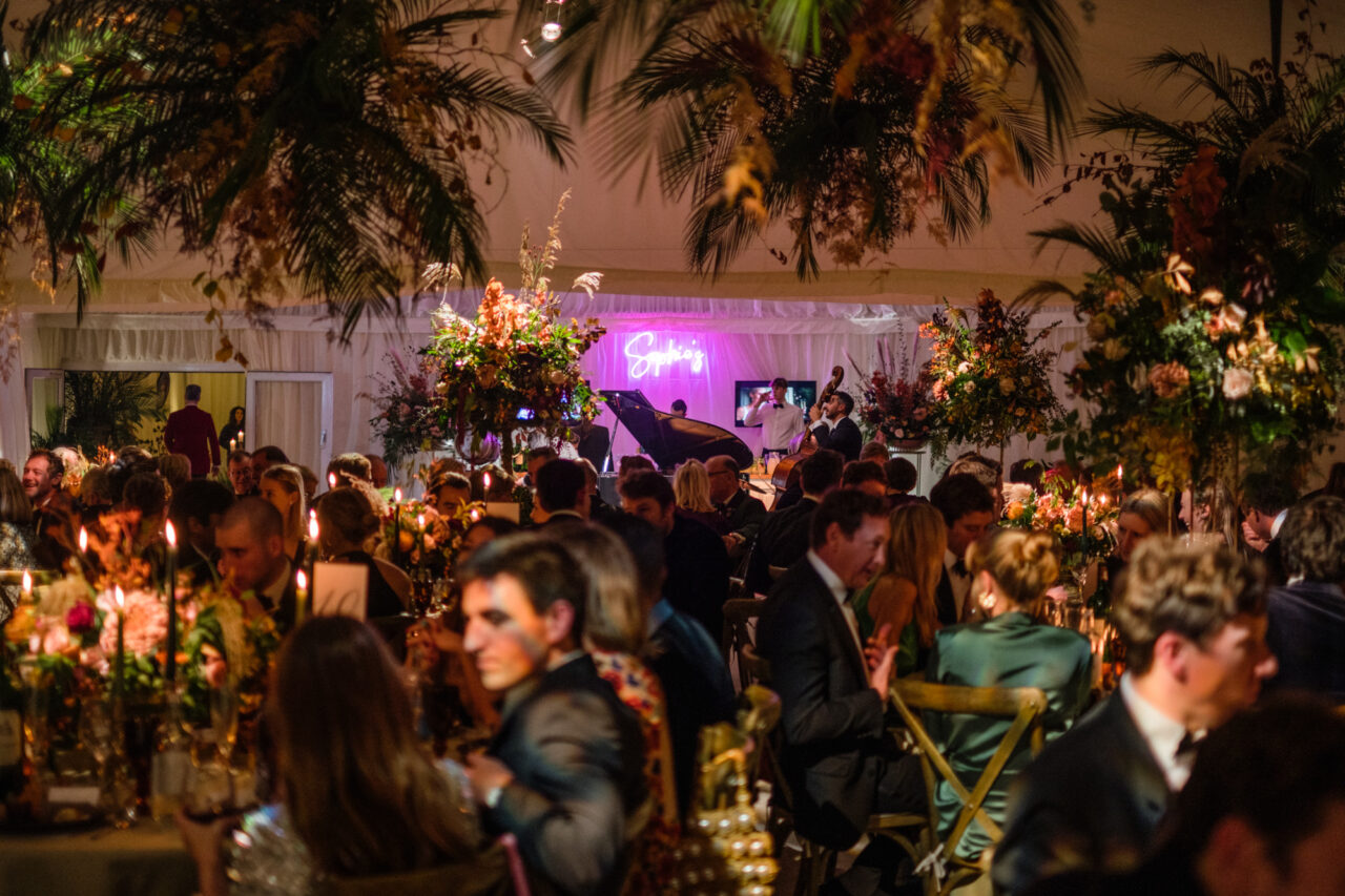 A wedding reception in a marquee with flowers and a jazz band playing.