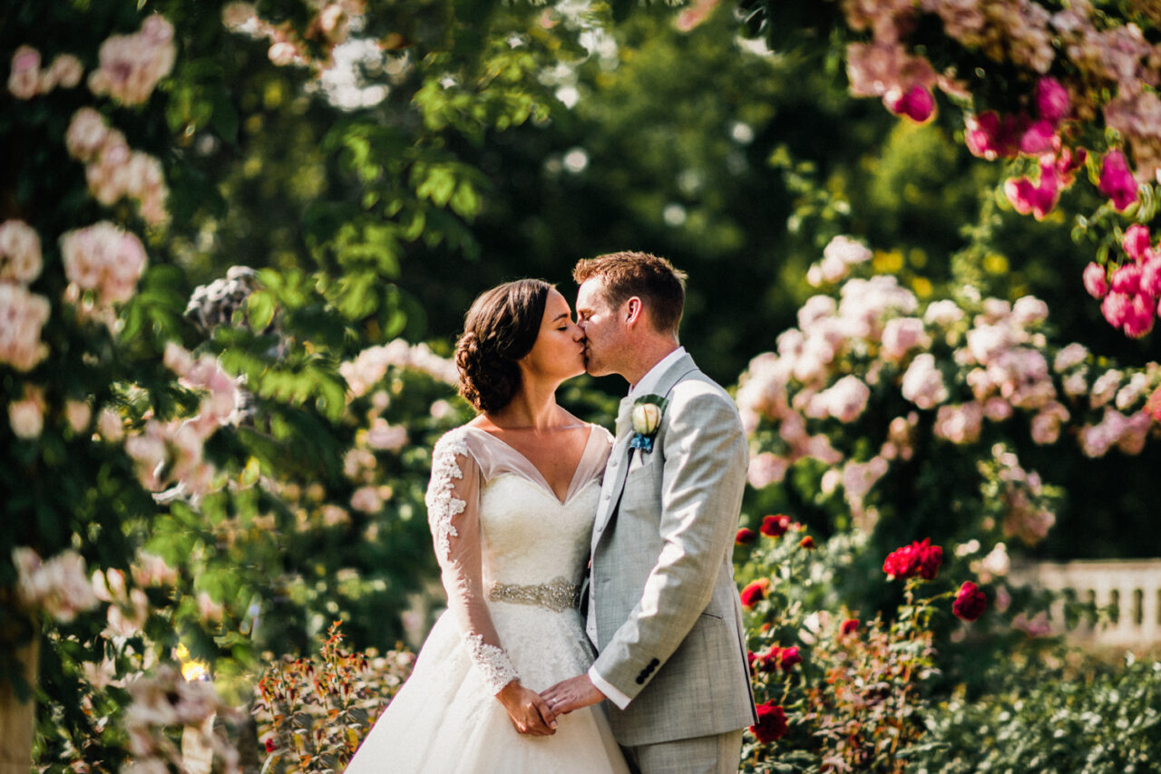 A couple kiss on their wedding day in Richmond, London. They are surrounded by flowers.