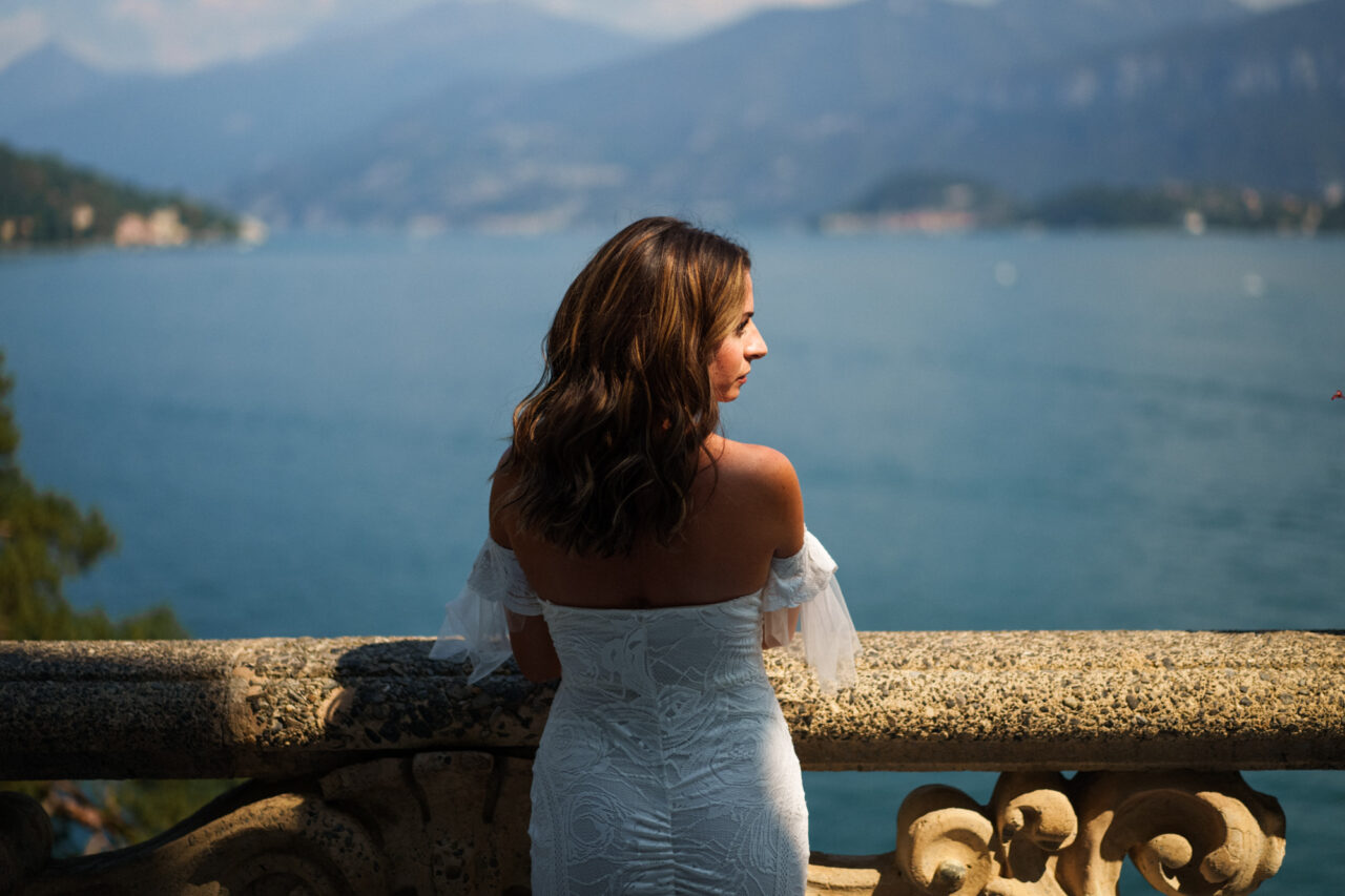 A bride wearing a beautiful white wedding dress looks out at the lake from Villa del Balbianello.