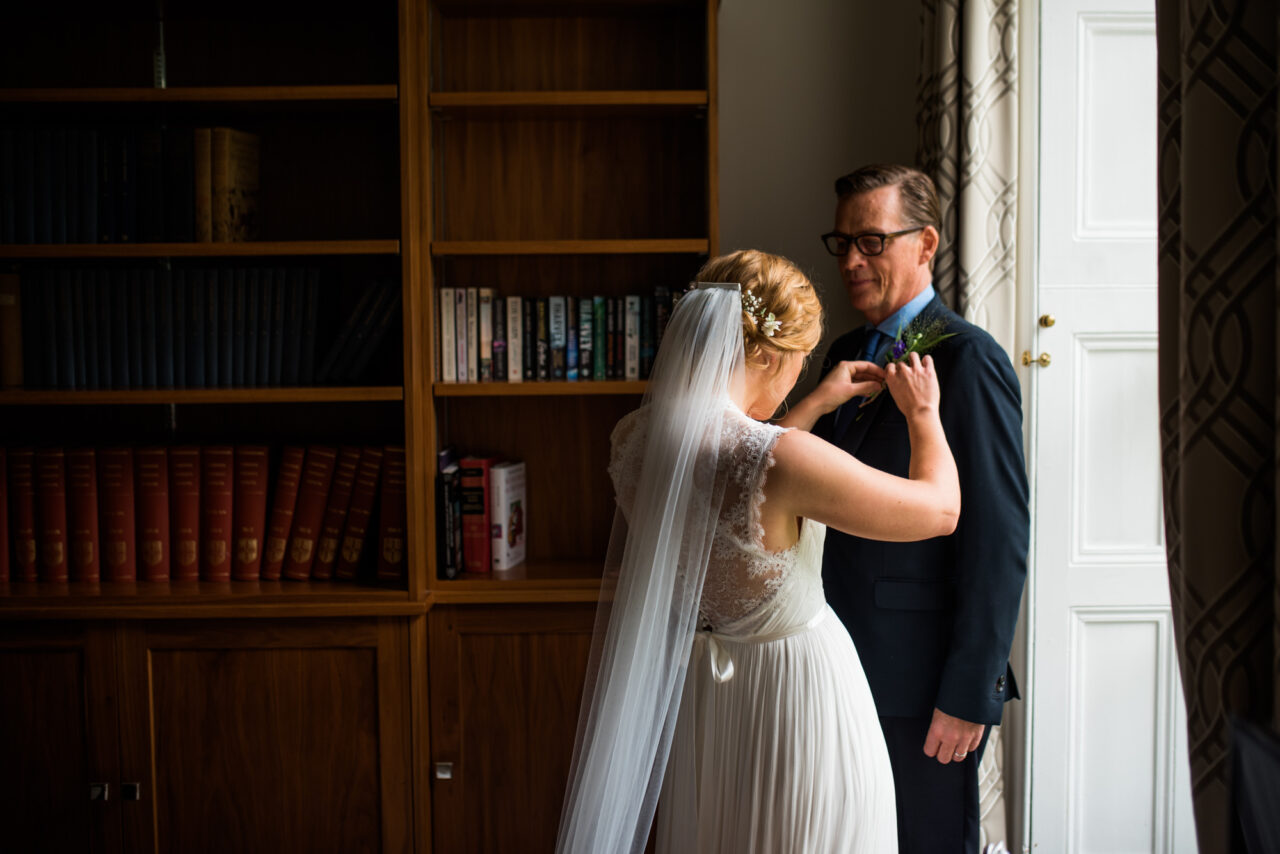 Documentary wedding photo of a bride adjusting her father's buttonhole flower.