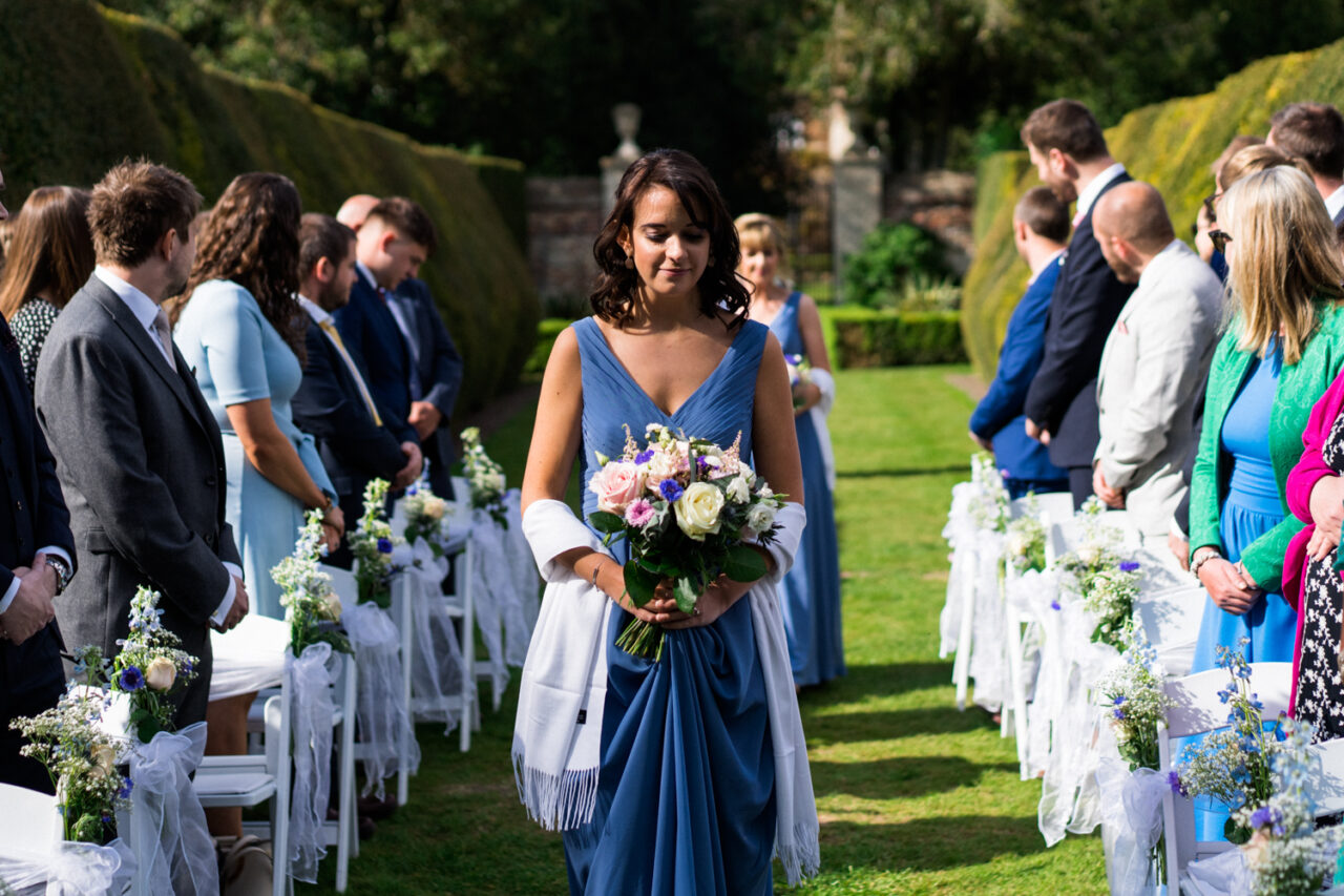 Wedding photo of a bridesmaid walking down the aisle in Hockwold Hall, Hockwold cum Wilton, Norfolk, England.