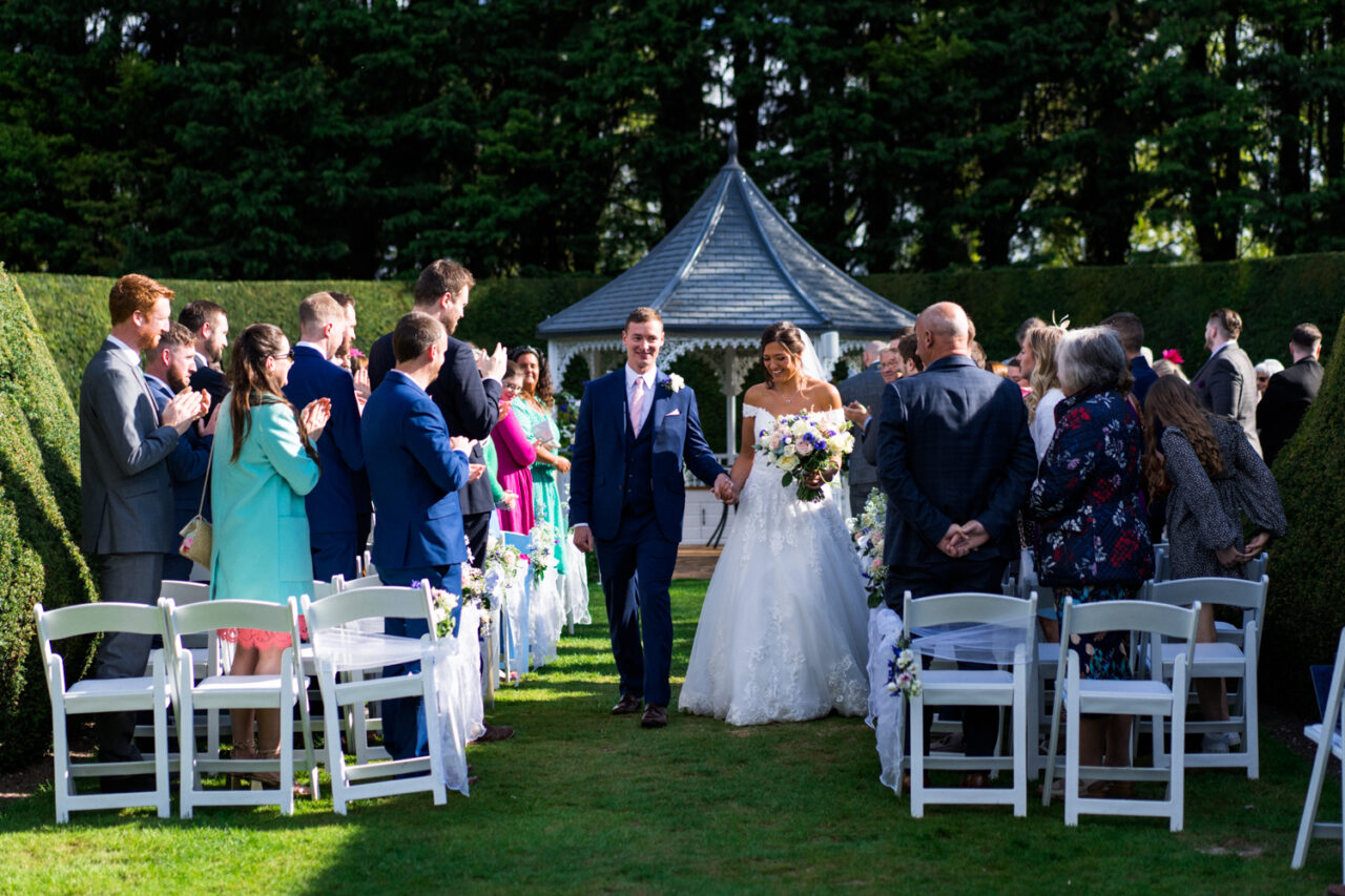 A bride and groom walk down the aisle after their outside ceremony at Hockwold Hall.