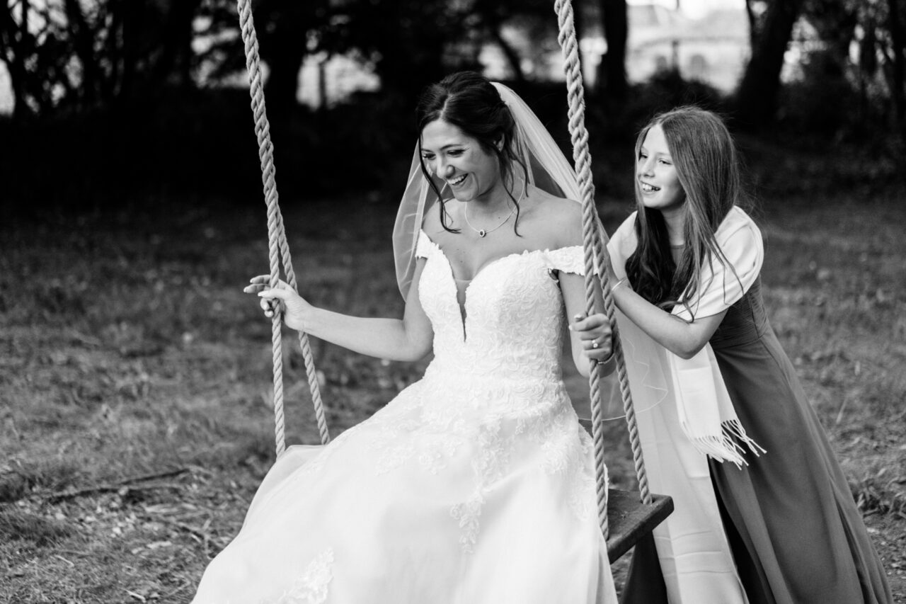 A bride and her flower girl play on the swing at Hockwold Hall - the flower girl is pushing the bride.