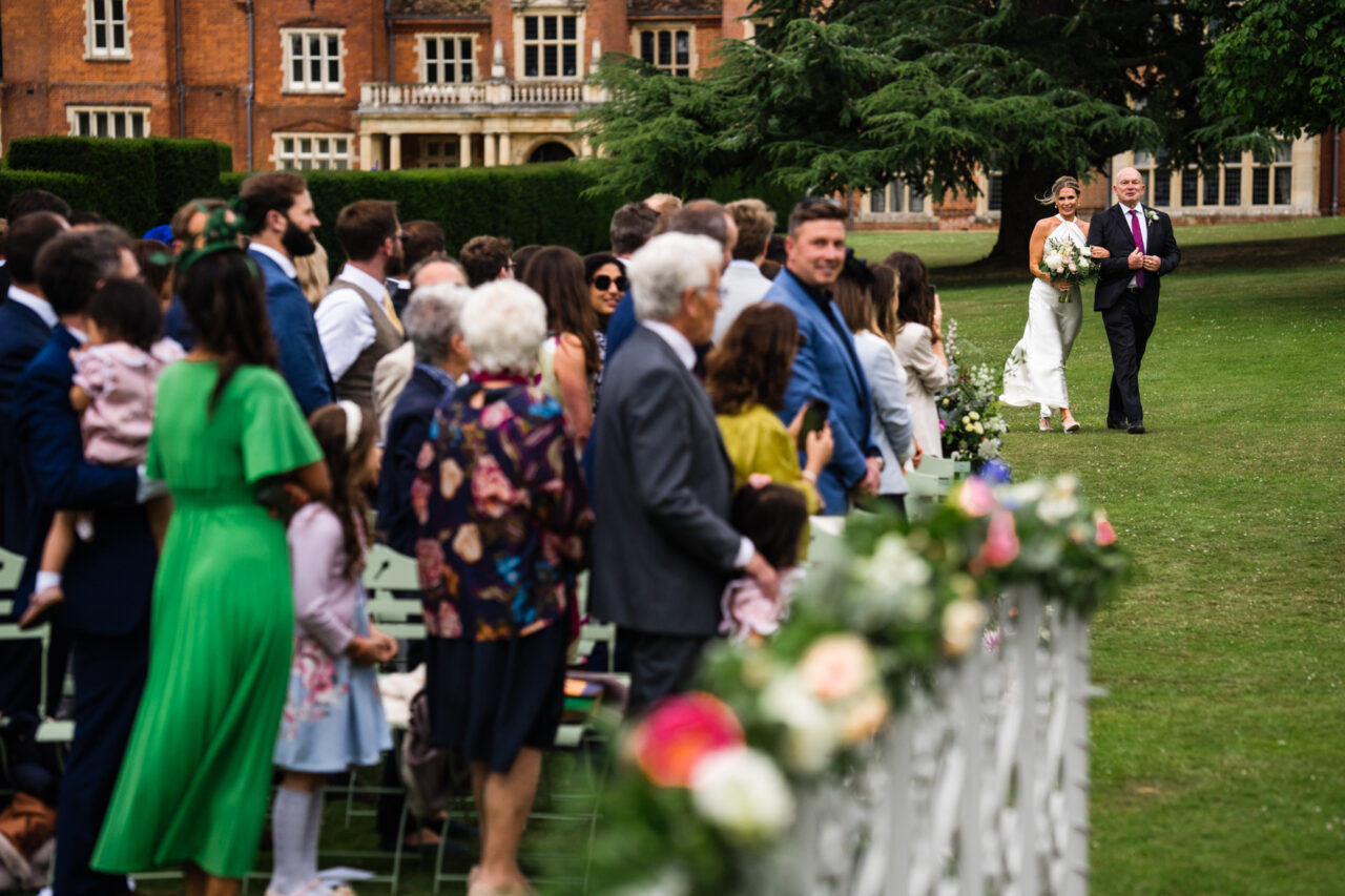 Longstowe Hall Wedding Photography. Bride and her father arriving at an outside ceremony at Longstowe Hall.