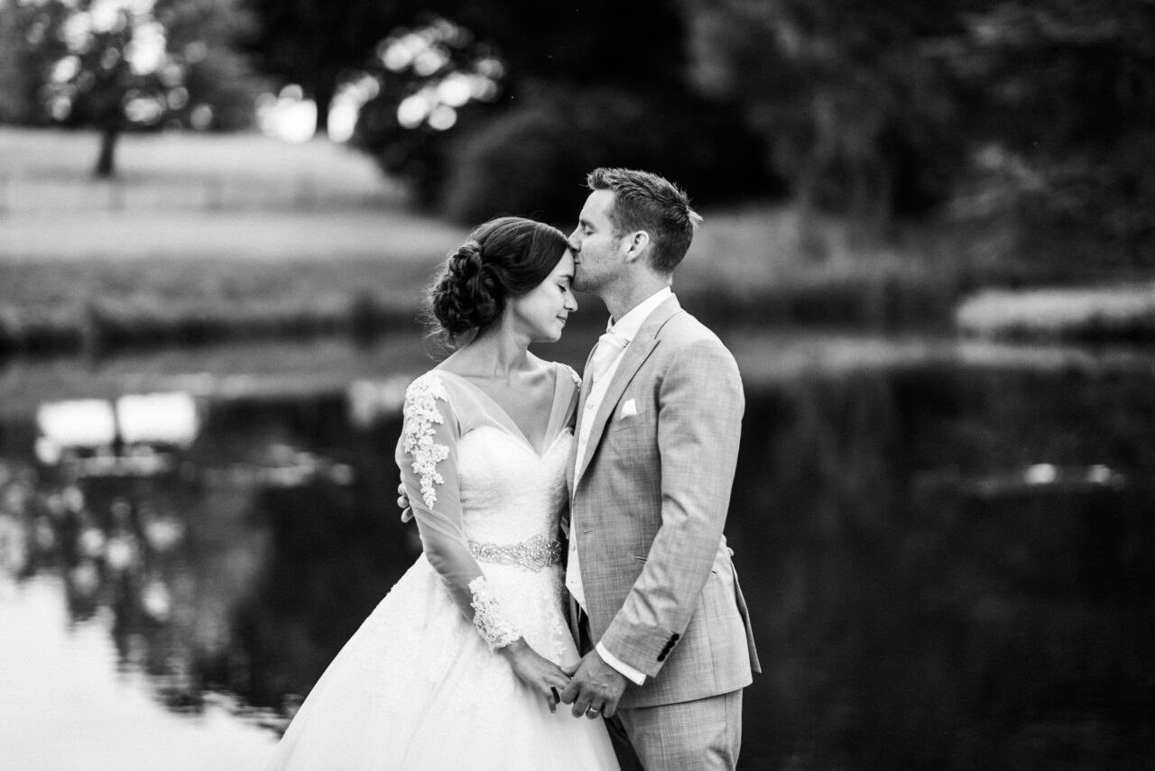 A couple kiss on their wedding day by the lake at Longstowe Hall.