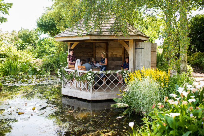 Guests relaxing in the wooden summerhouse over the pond in the gardens at South Farm wedding venue Cambridgeshire.