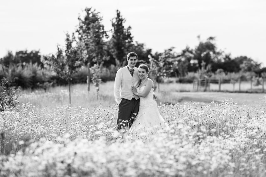 Bride and groom walking through a wildflower meadow at South Farm wedding venue Cambridgeshire.