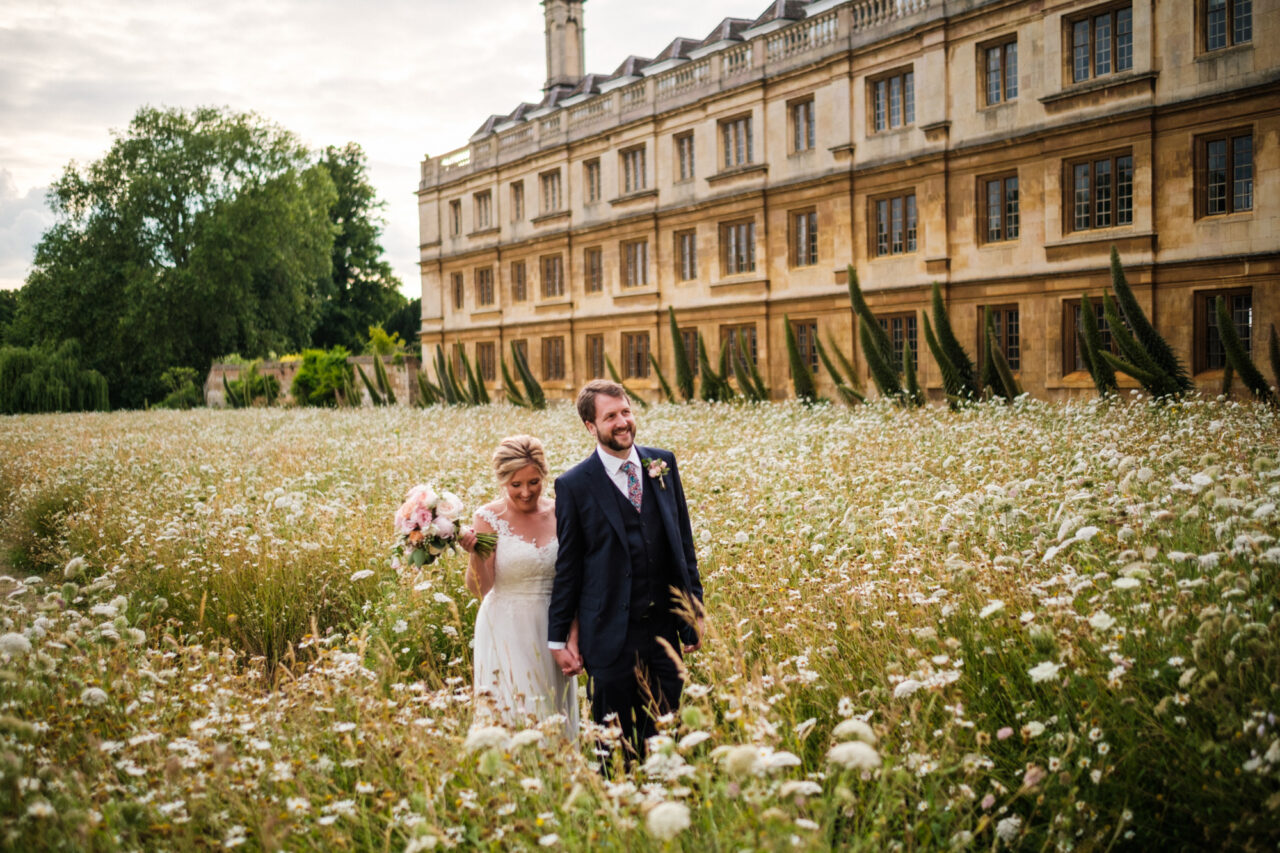 A bride and groom walk in fields of flowers in King's College in Cambridge.