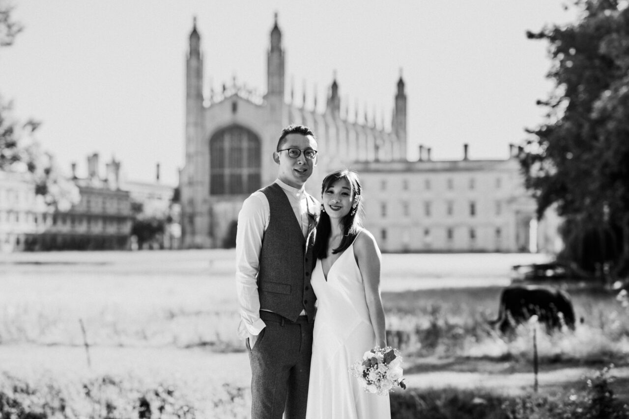 A couple post at The Backs in Cambridge with King's College and a cow in the background.