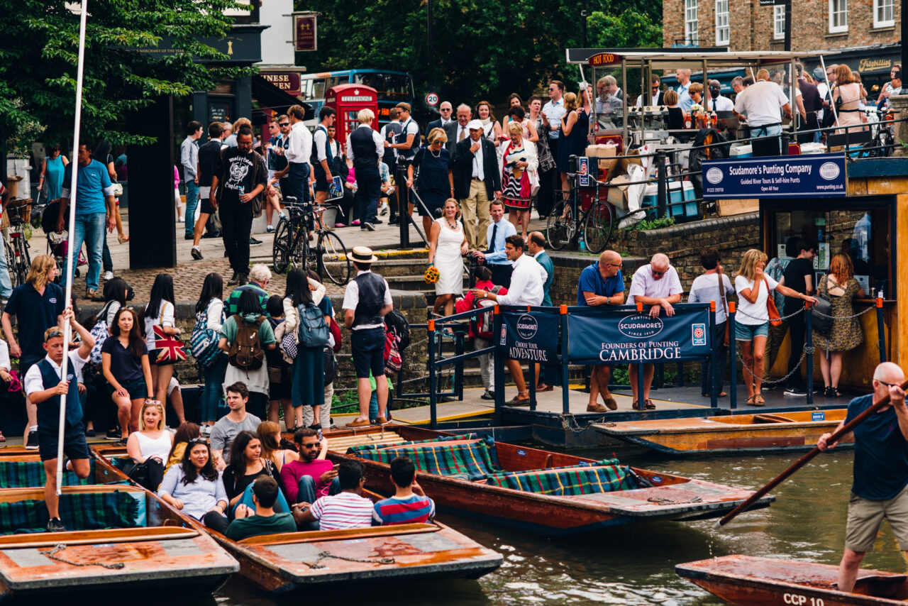 A bride stands in the middle of a crowd of people on the banks of the River Cam.