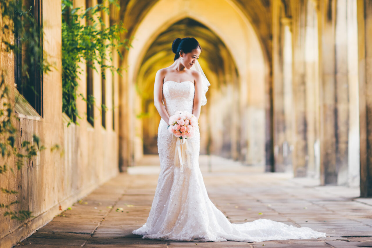 A bride poses with a bouquet of flowers in the cloisters at St John's College in Cambridge.