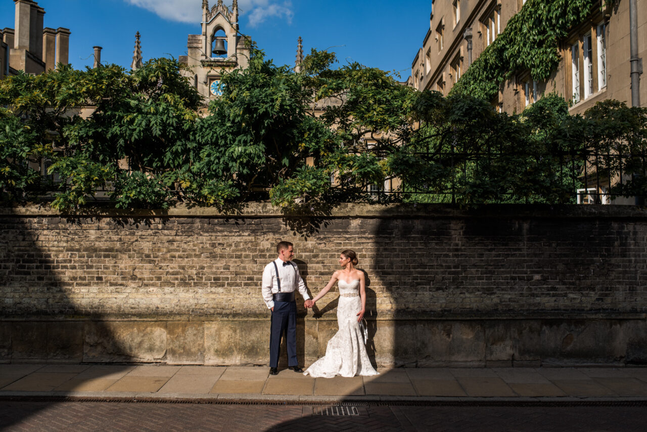 A couple hold hands on a street in Cambridge, surrounded by shadows.