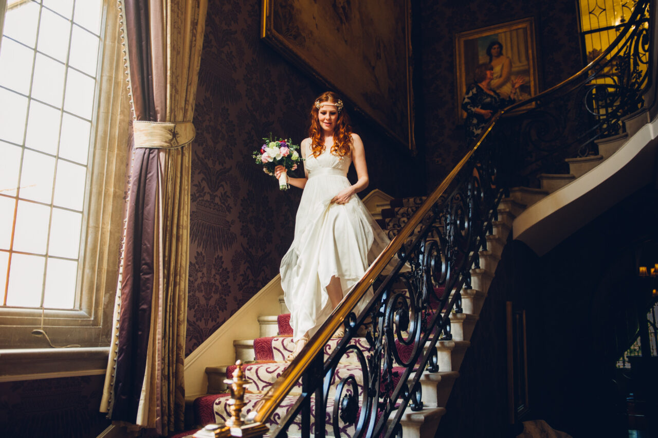 Cambridge wedding photographer - a bride walking down stairs holding some flowers.