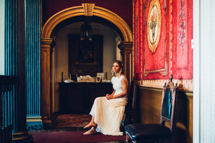 Bride seated in an elegant red hallway at Island Hall wedding venue Cambridgeshire.
