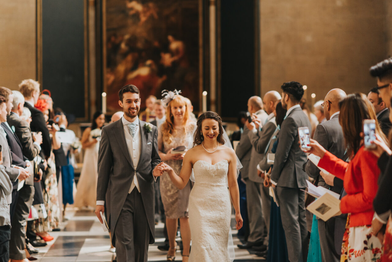 A bride and groom hold hands as they walk back down the aisle after their wedding at King's.