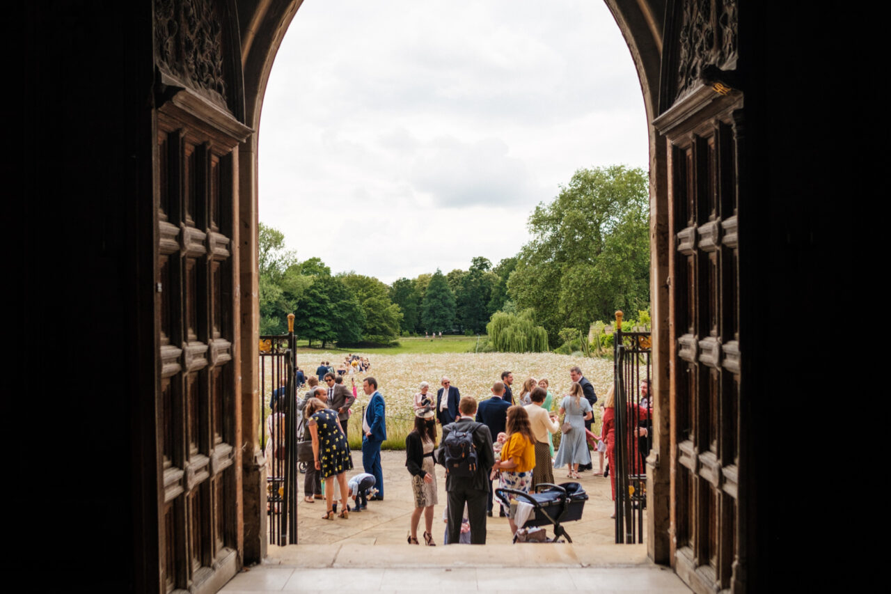 A view from inside King's College Chapel - the large doors are open and outside you can see wedding guest and the field of wild flowers.