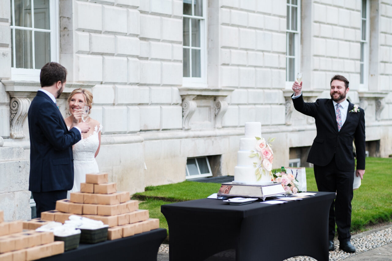 A best man toasts the bride and groom outside in the grounds of King's College.