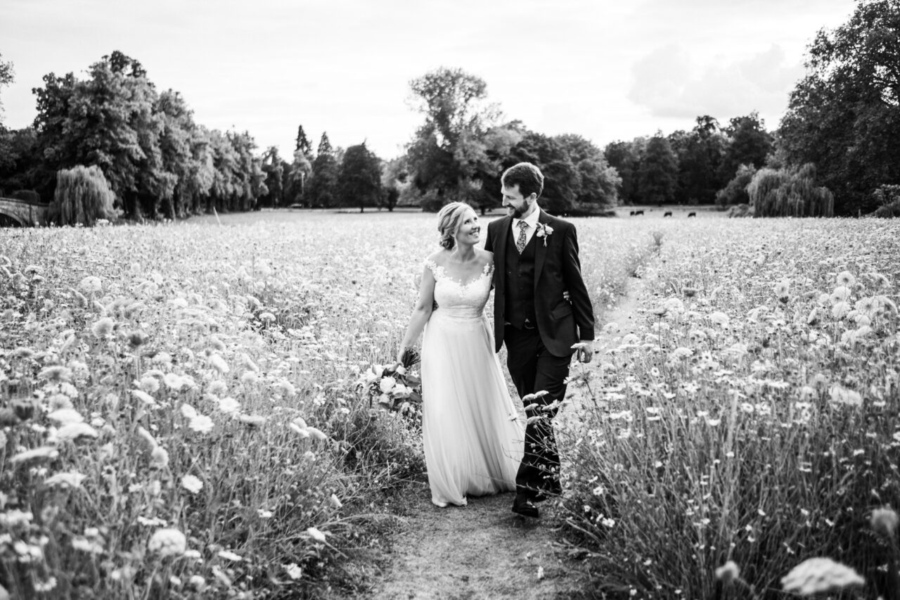 A bride and groom walk through wild flowers in Cambridge.