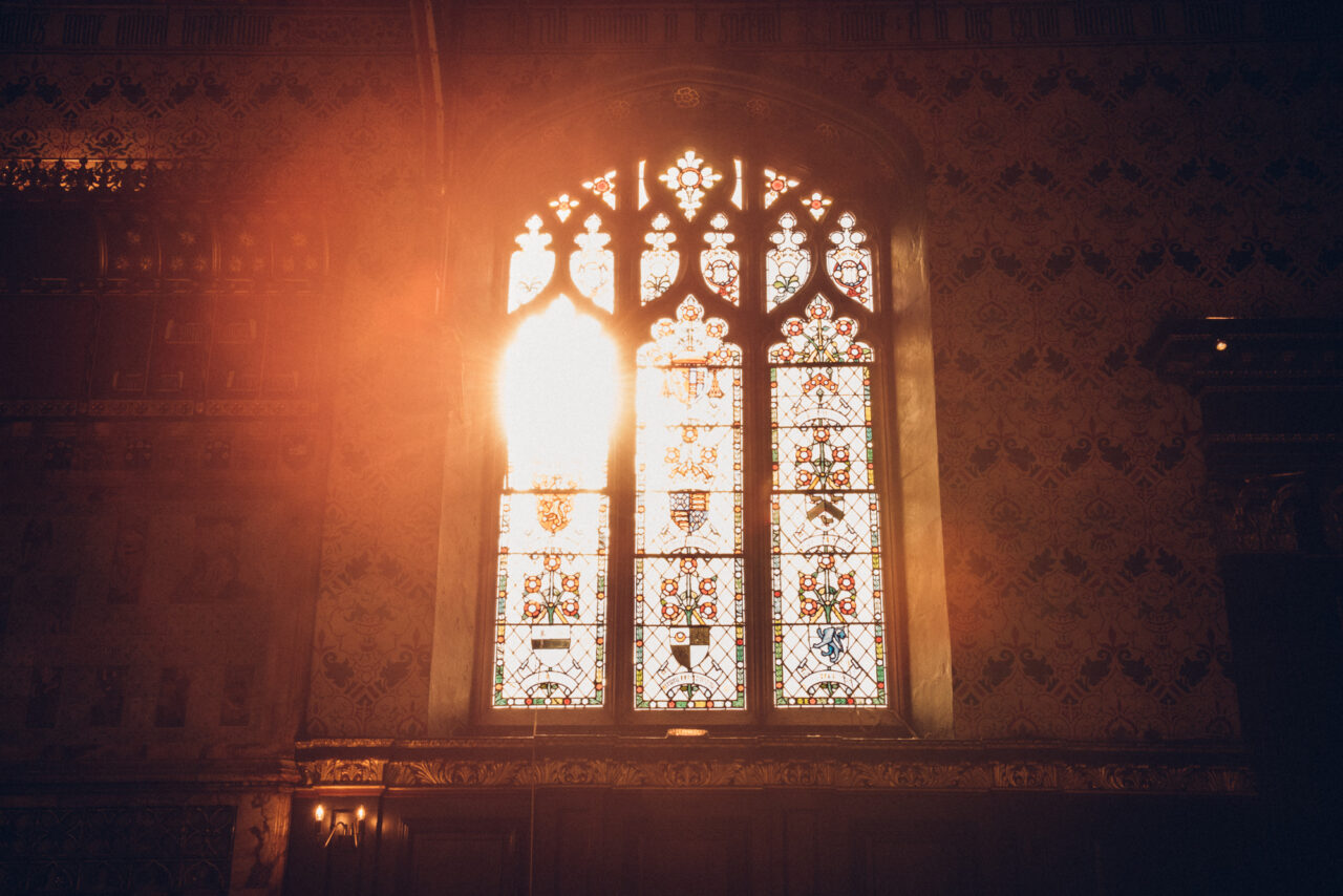 The sun bursts through the stained glass window in The Old Hall at Queens' College.