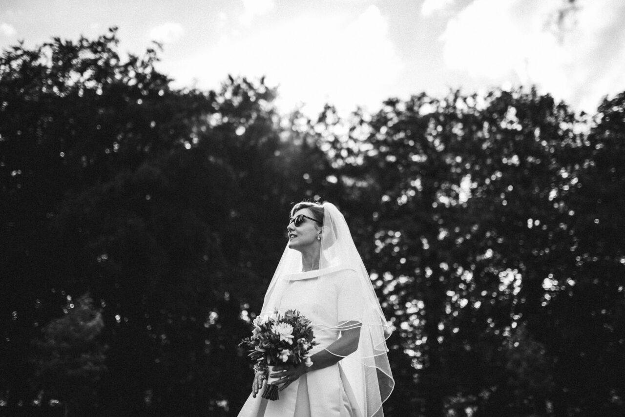 A bride in the Fellows Garden at Queens' College wearing sunglasses.