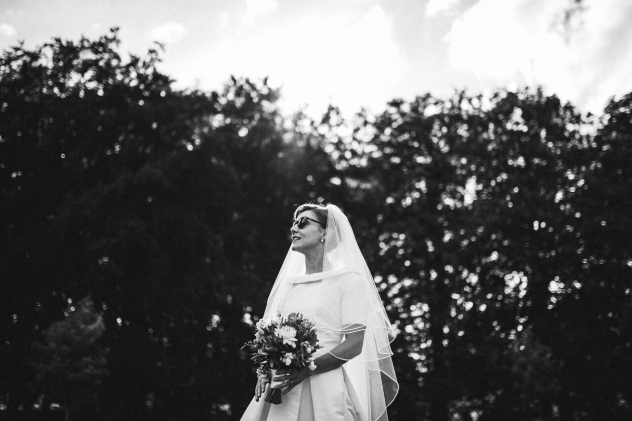 A bride in the Fellows Garden at Queens' College wearing sunglasses.