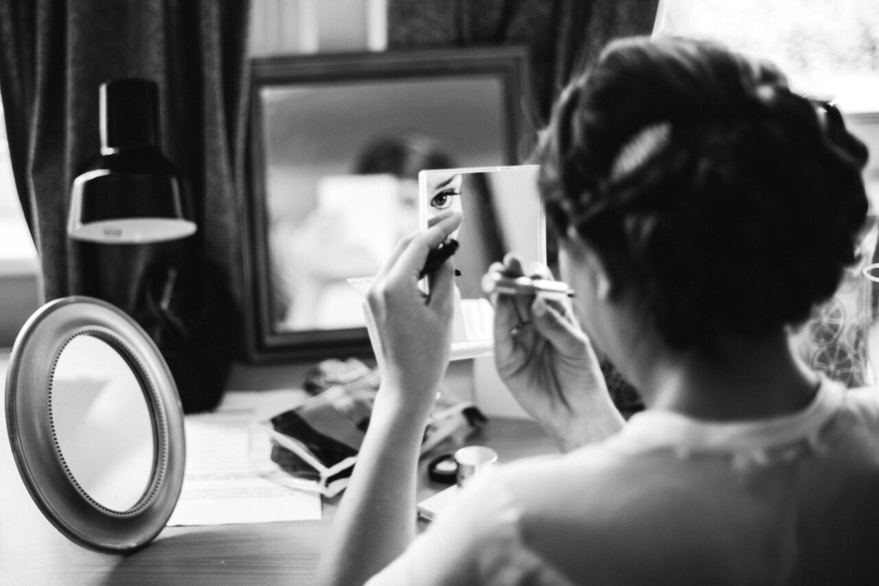 A bride is putting on lipstick in a mirror.