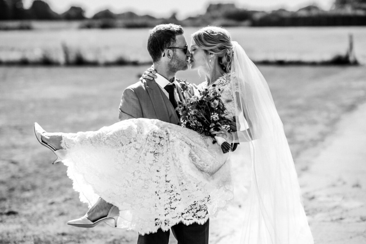 A black and white photo of a groom lifting up his bride in a field.