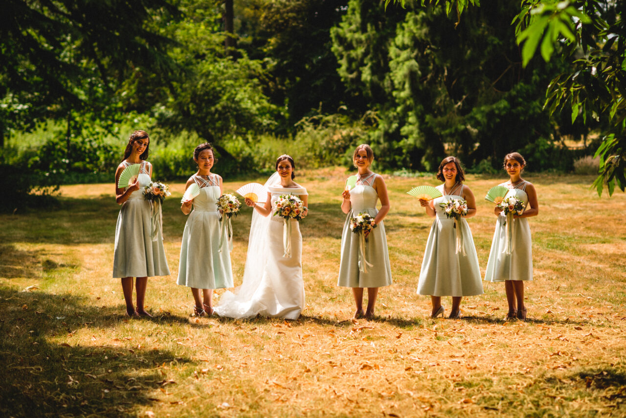 A bride with her 5 bridesmaids stand in line holding paper fans.