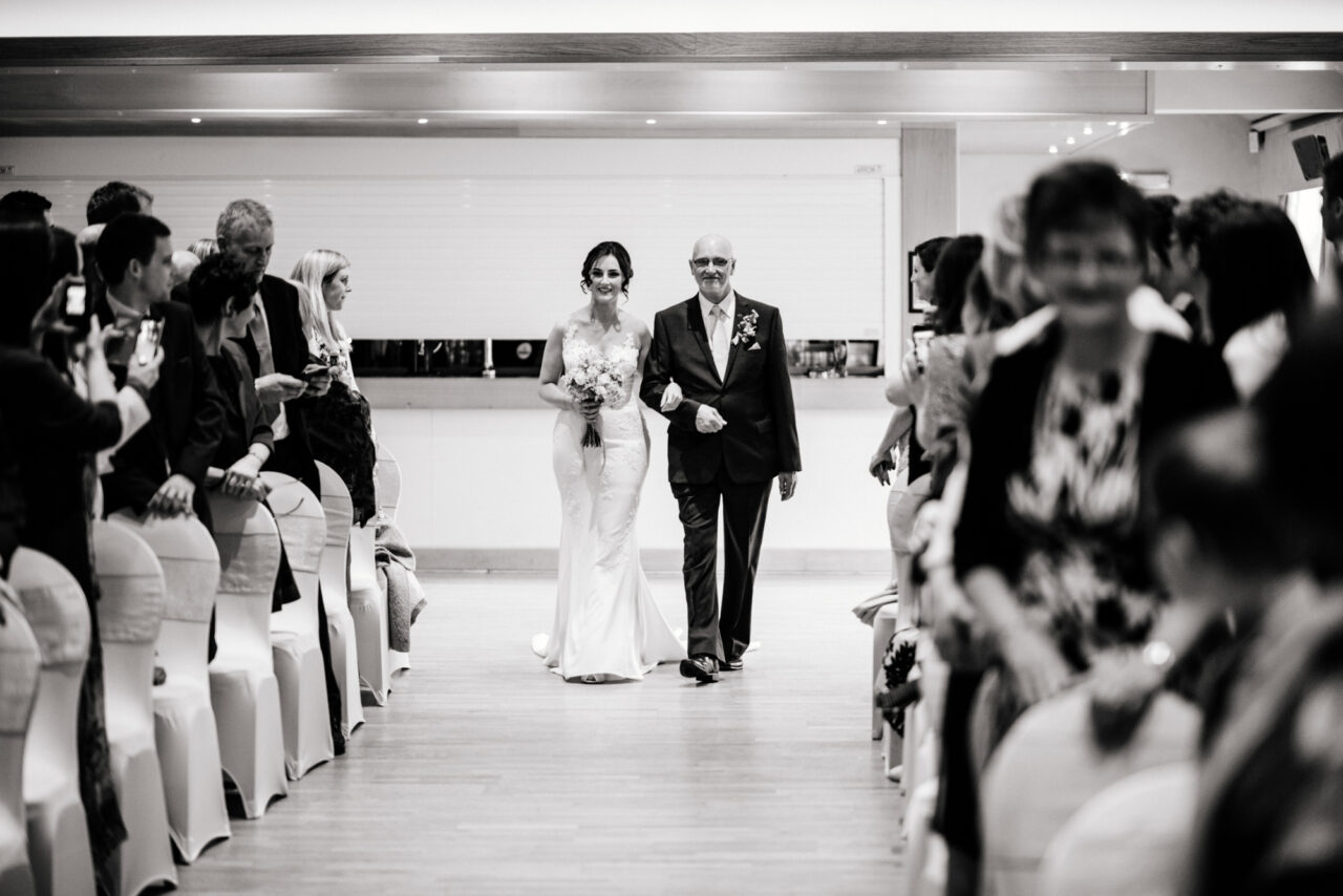 A bride and her father walk down the aisle at Slepe Hall in St Ives, Cambridgeshire.