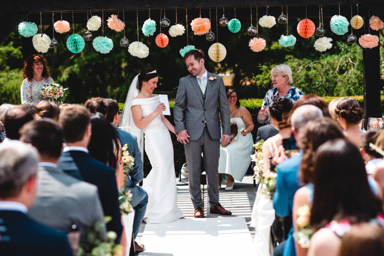 A bride and groom hold hands during an outdoor wedding ceremony at Swynford Manor in Newmarket.