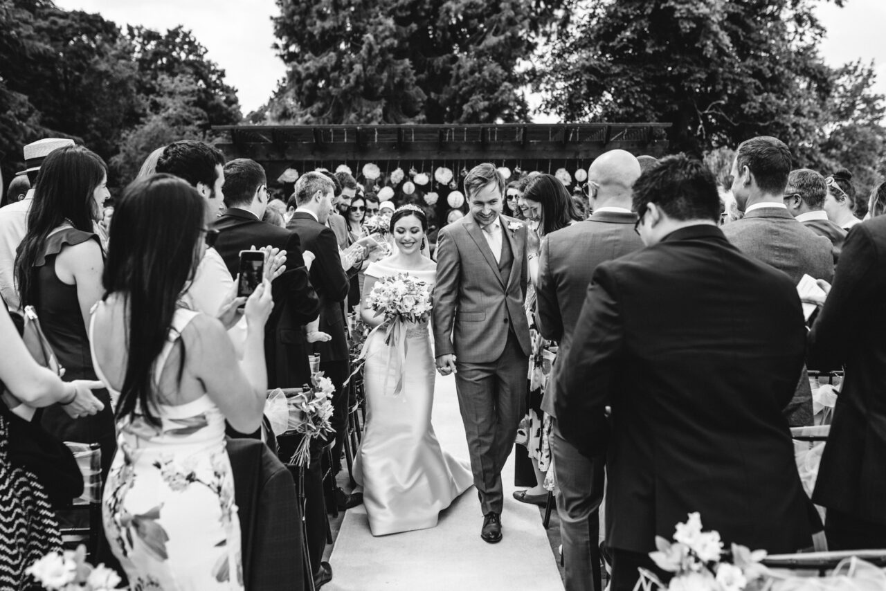 A bride and groom walk back down the aisle outside at Swynford Manor.