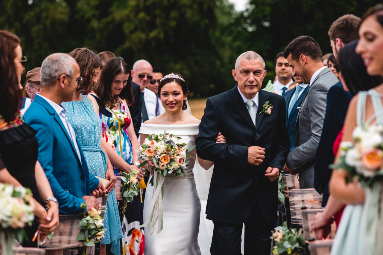 A bride and her father walk down the aisle at an outdoor wedding at Swynford Manor.