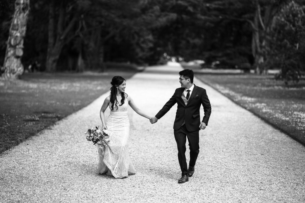 A young couple run holding hands through Cambridge University Botanic Garden.