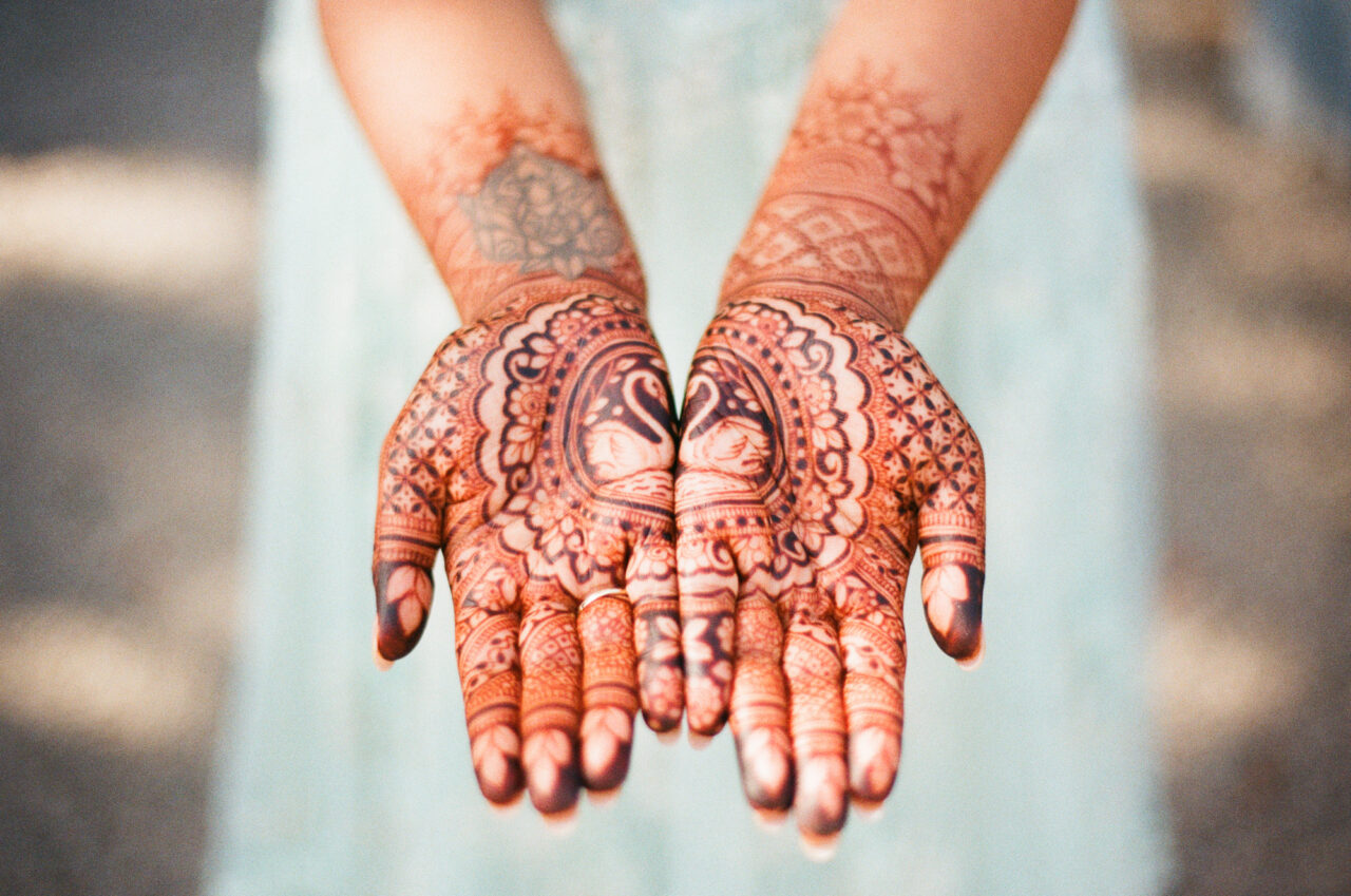 35mm film photograph of a bride's hands decorated with Indian henna patterns.