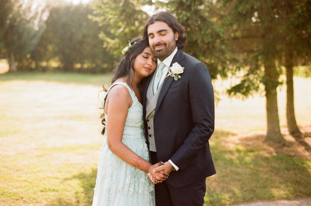 35mm film wedding photo of a couple embracing with sunlight and trees behind them.