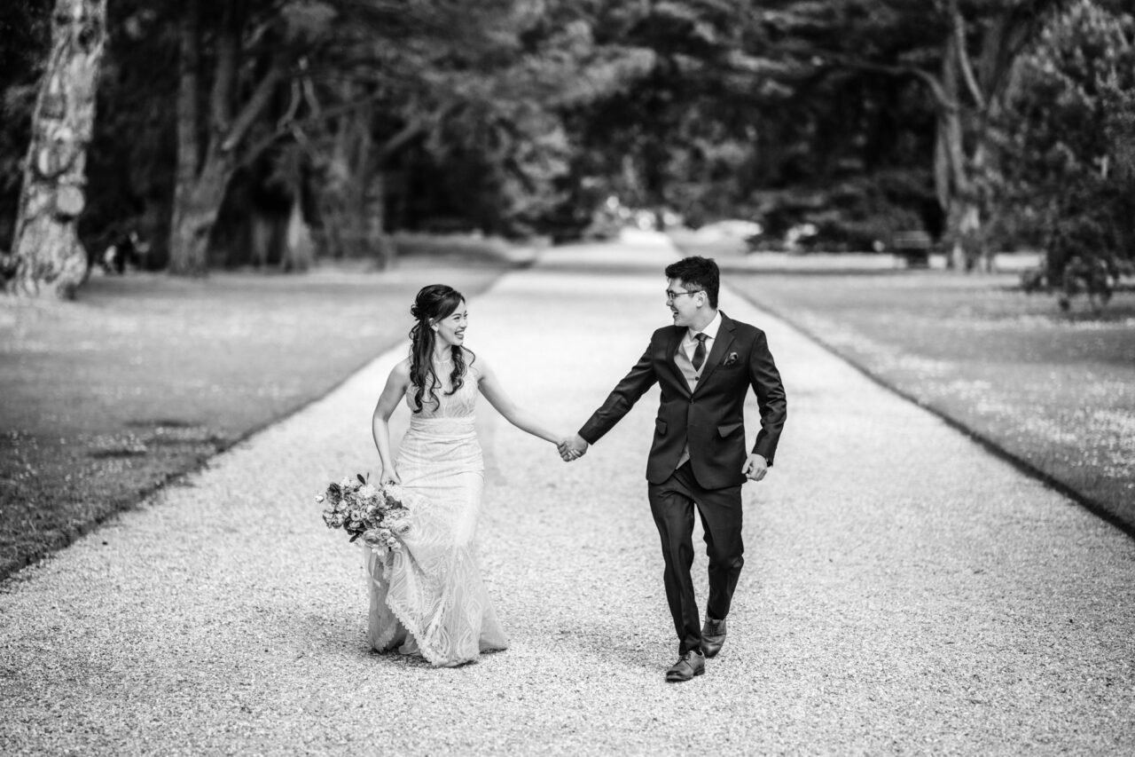 Black and white wedding photo of a couple holding hands and running towards the camera.