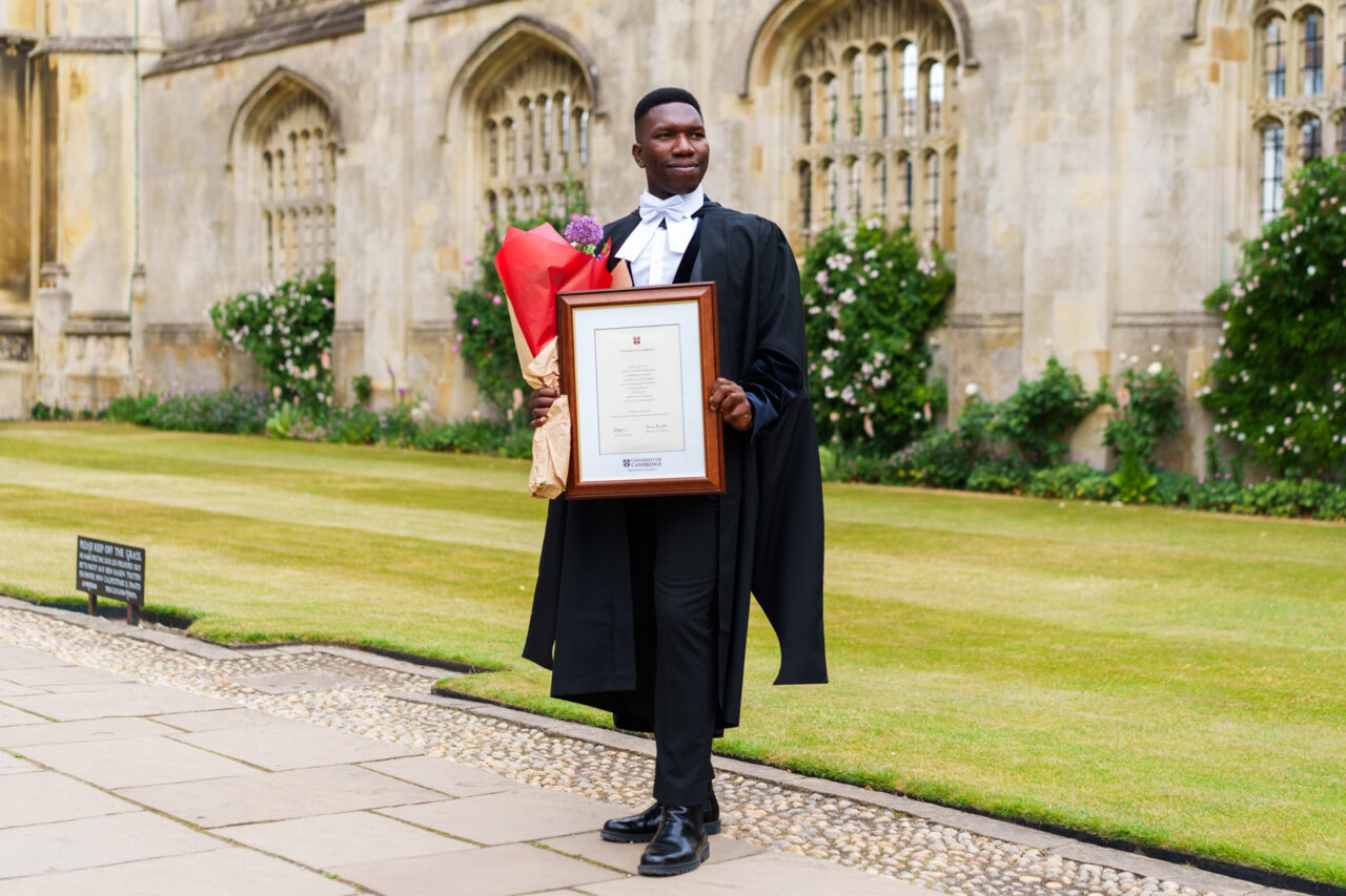 Photo of Cambridge graduate at King's College in Cambridge. He is holding a certificate and flowers.