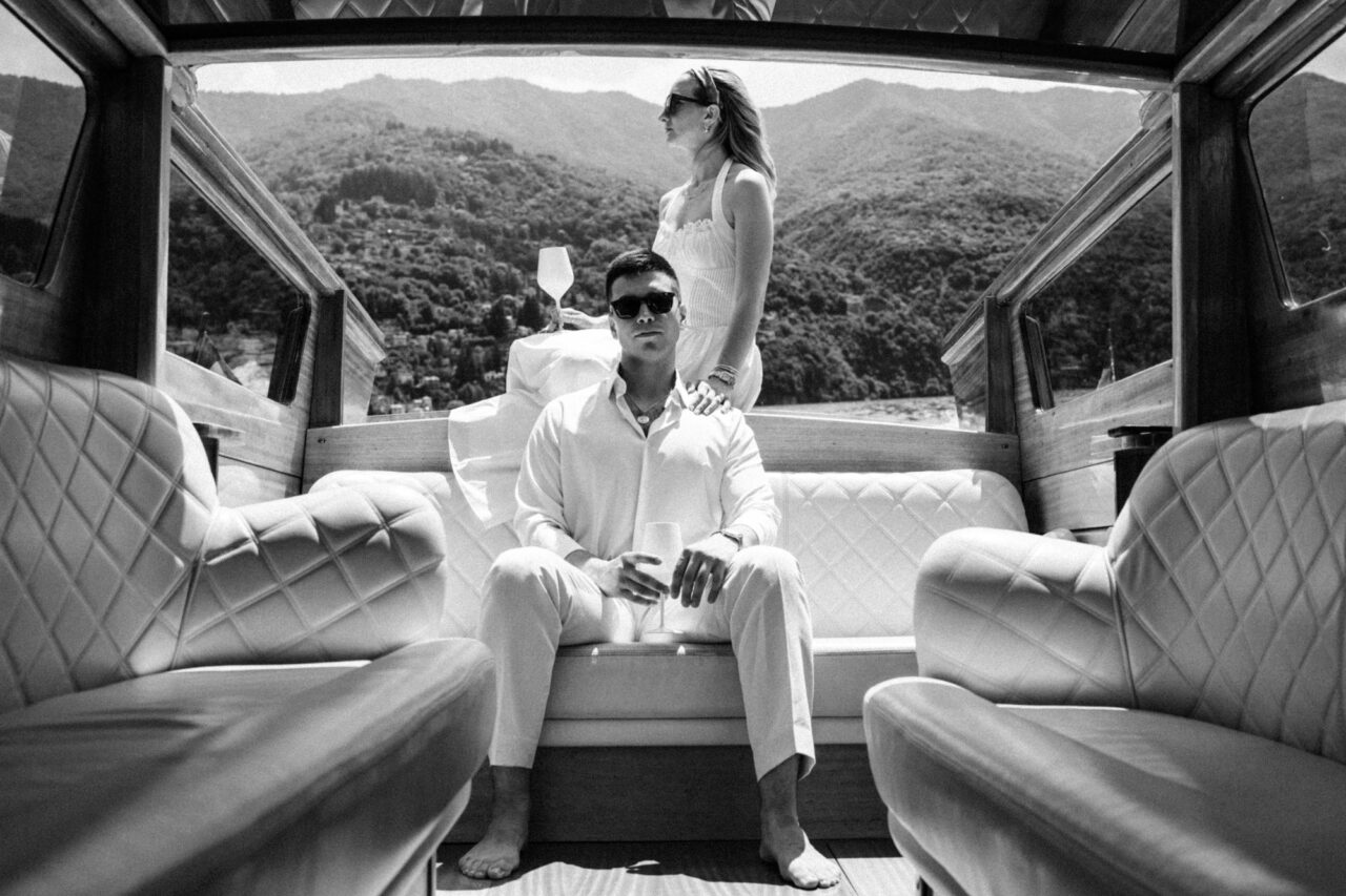 Man and a women pose on the back of a classic boat on Lake Como.