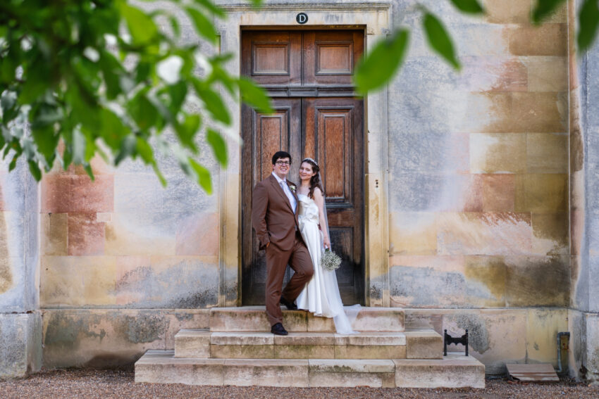 A bride and groom pose on the steps at Downing College in Cambridge.