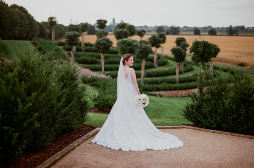 Portrait of a bride at The Old Hall in Ely. In the background are young trees and Ely Cathedral.