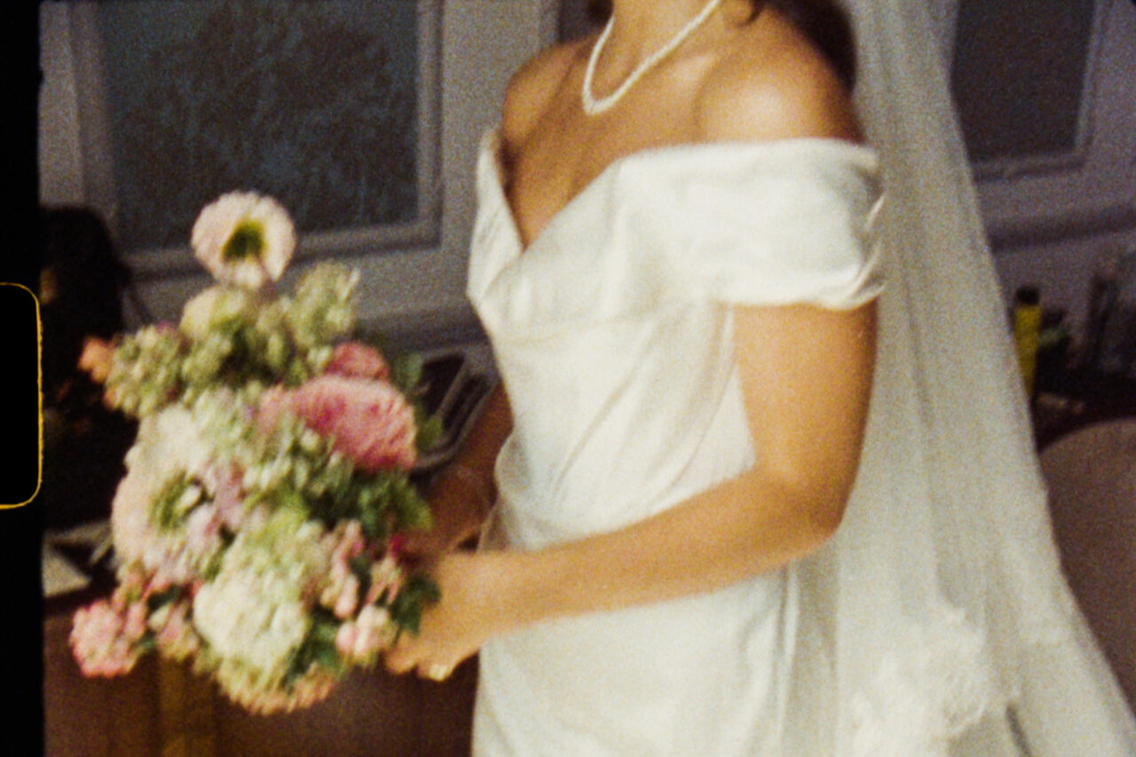 Frame from a Super 8 wedding film - a bride in a white dress hold a bouquet of flowers.