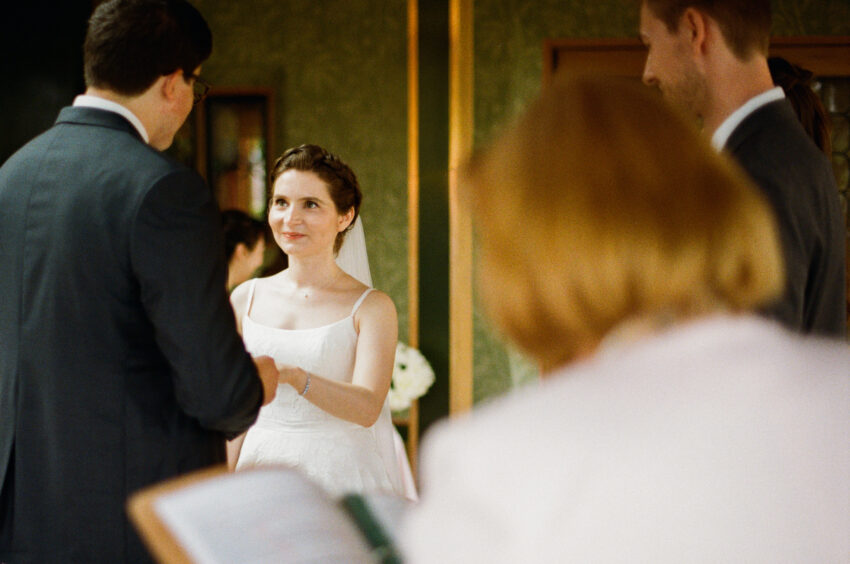 A bride and groom say their vows as they face each other in this warm analogue photograph.