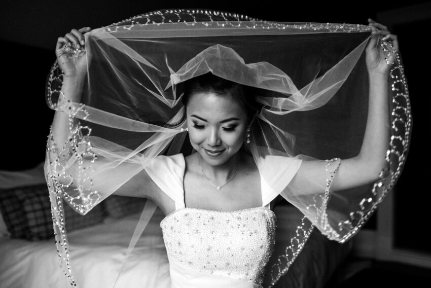 Black and white bridal portrait captured by a Lincolnshire wedding photographer, showing a quiet, intimate moment as the bride lifts her veil above her head before the ceremony.