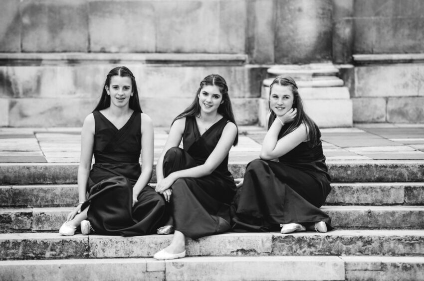 Three flowergirls sit together on some steps at a wedding.